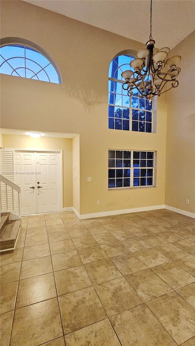 tiled entryway featuring a notable chandelier, stairway, a high ceiling, and baseboards