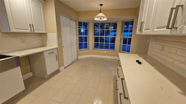 kitchen featuring hanging light fixtures, light tile patterned flooring, white cabinetry, and light stone counters