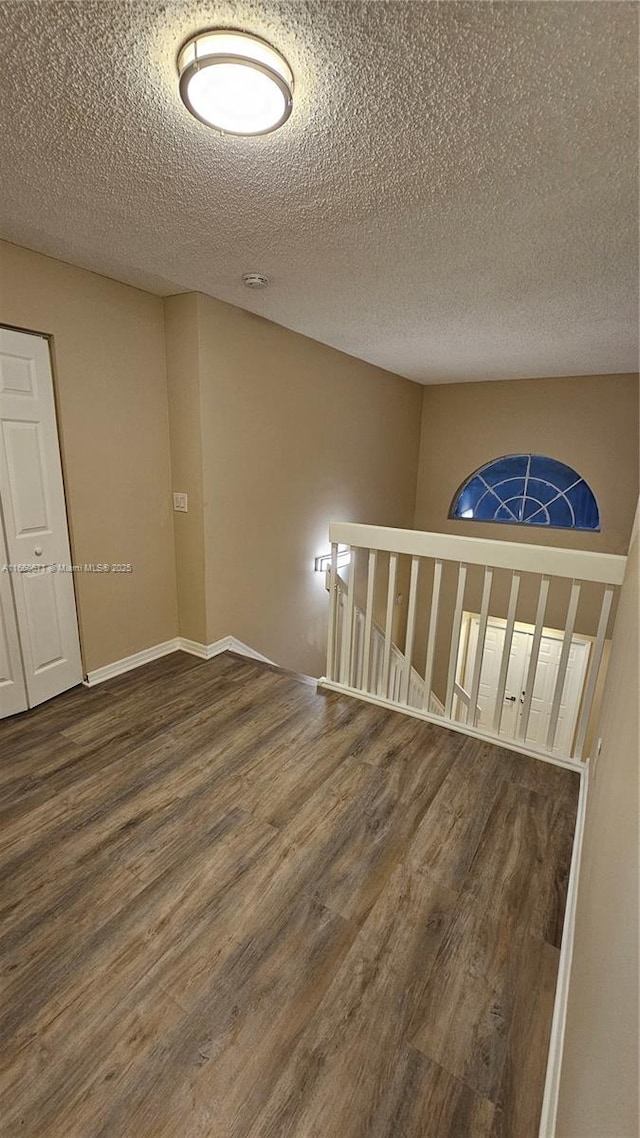 unfurnished room featuring a textured ceiling, baseboards, and wood finished floors