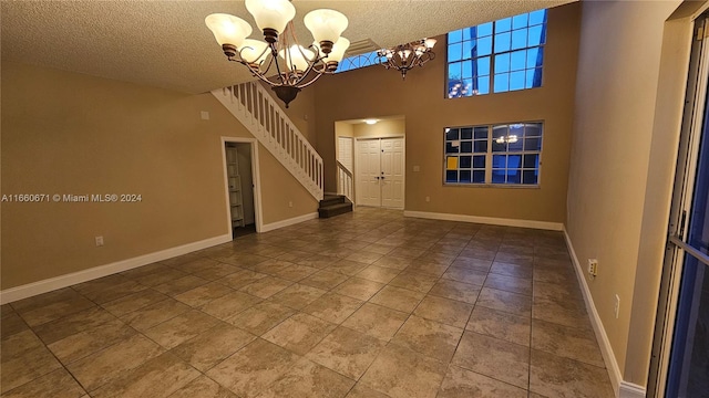 tiled empty room featuring a textured ceiling, a high ceiling, and a notable chandelier