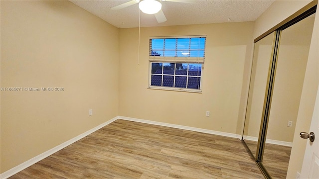 unfurnished bedroom featuring a ceiling fan, baseboards, light wood-style flooring, a closet, and a textured ceiling