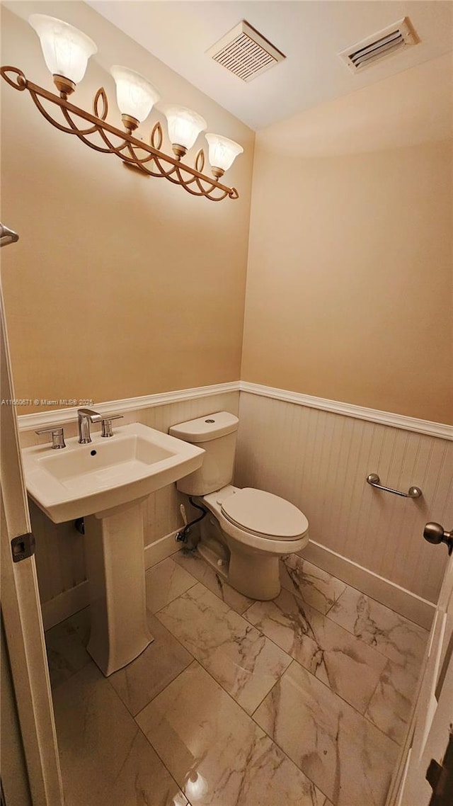 half bath with toilet, visible vents, marble finish floor, and wainscoting