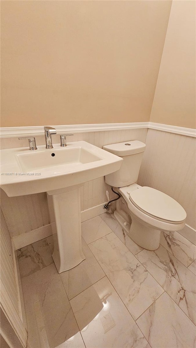 half bath with a wainscoted wall, toilet, and marble finish floor