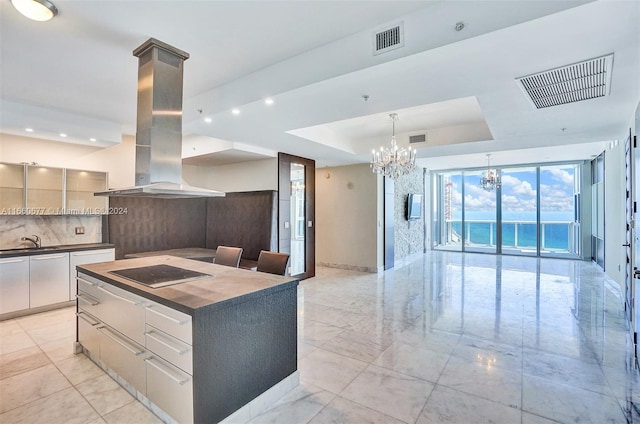 kitchen featuring black electric stovetop, a raised ceiling, an inviting chandelier, island exhaust hood, and a large island