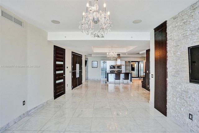 hall with a raised ceiling and an inviting chandelier