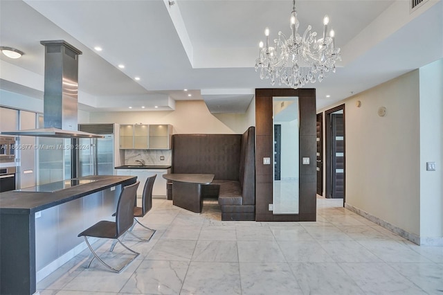 kitchen with backsplash, stainless steel appliances, a chandelier, a raised ceiling, and island exhaust hood