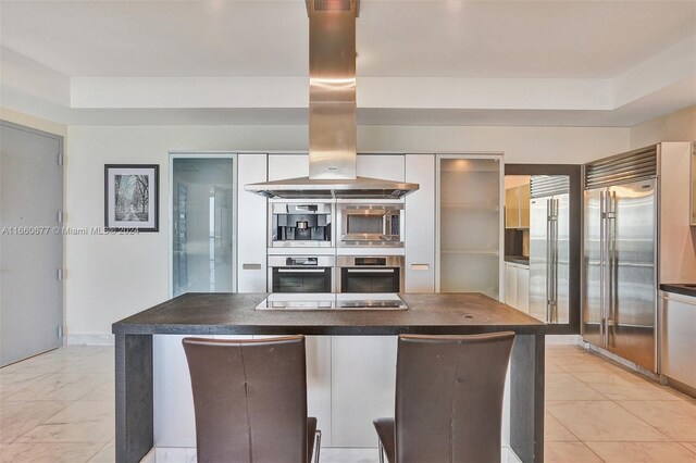 kitchen featuring island range hood, built in appliances, and white cabinetry