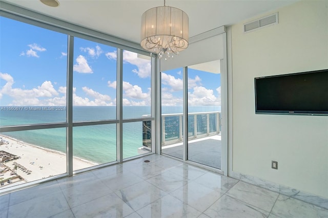 spare room with a wealth of natural light, a view of the beach, a chandelier, and a water view