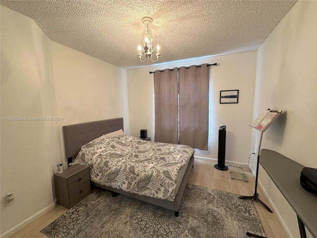 bedroom with an inviting chandelier, a textured ceiling, and light hardwood / wood-style floors