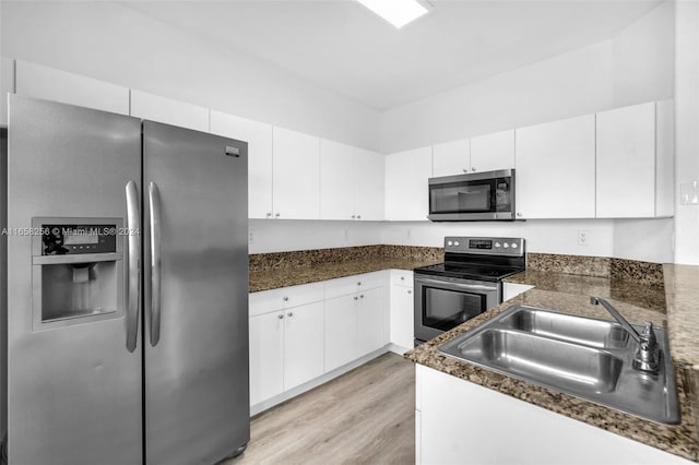 kitchen with white cabinetry, sink, light hardwood / wood-style flooring, dark stone counters, and appliances with stainless steel finishes