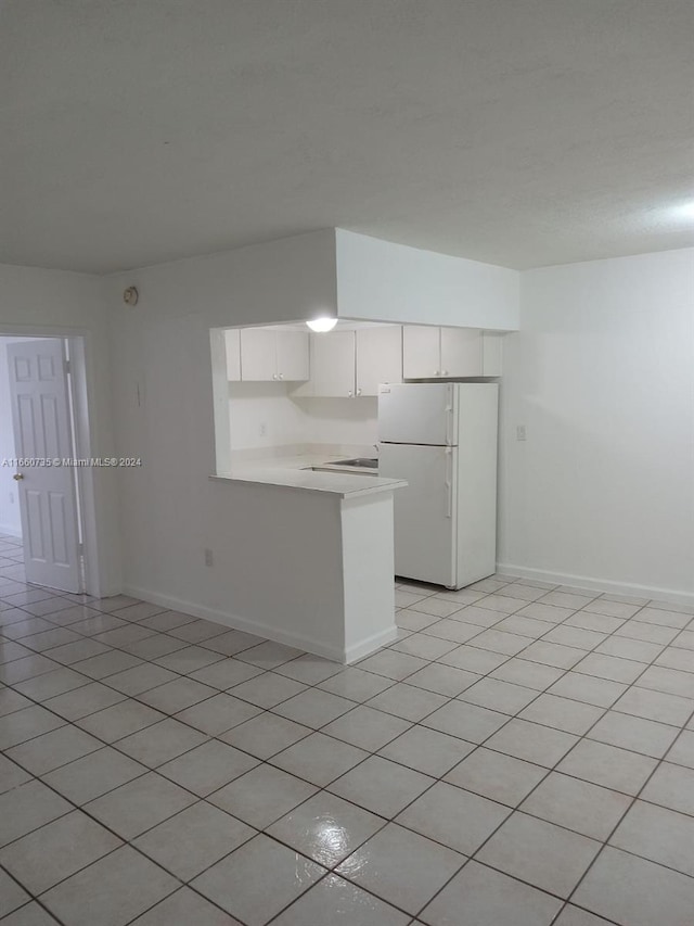 kitchen with light tile patterned flooring, white fridge, kitchen peninsula, and white cabinetry