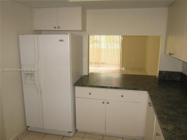 kitchen featuring white fridge with ice dispenser, light tile patterned floors, and white cabinetry