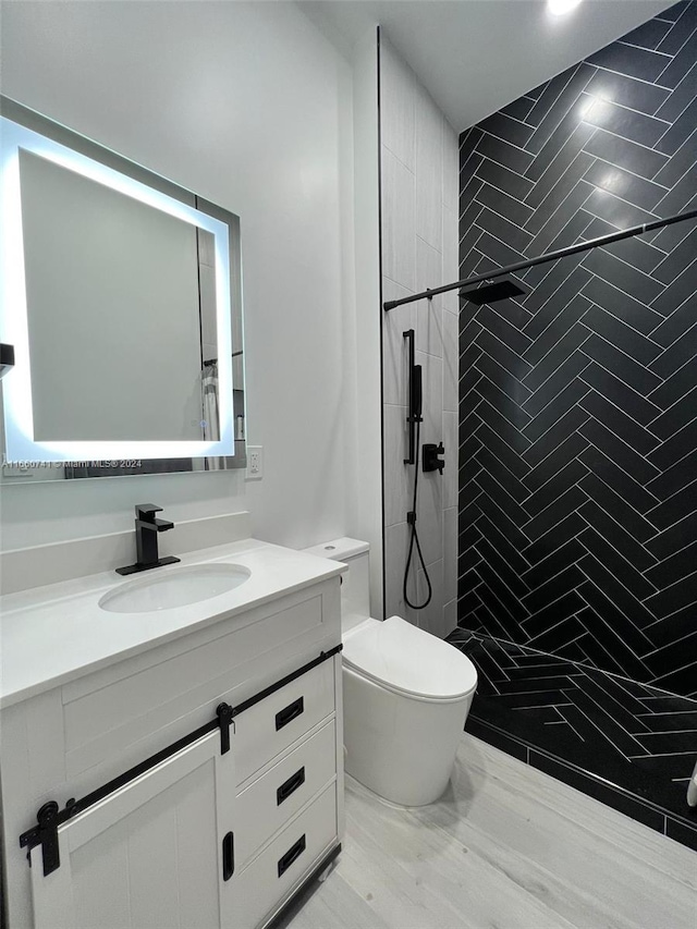 bathroom with a tile shower, vanity, toilet, and hardwood / wood-style flooring