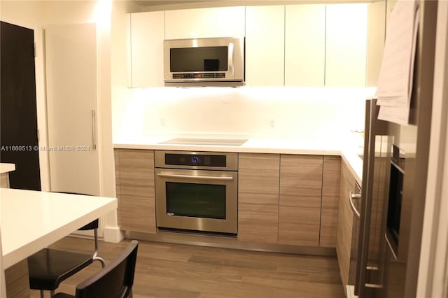 kitchen with stainless steel appliances, light wood-type flooring, and white cabinetry