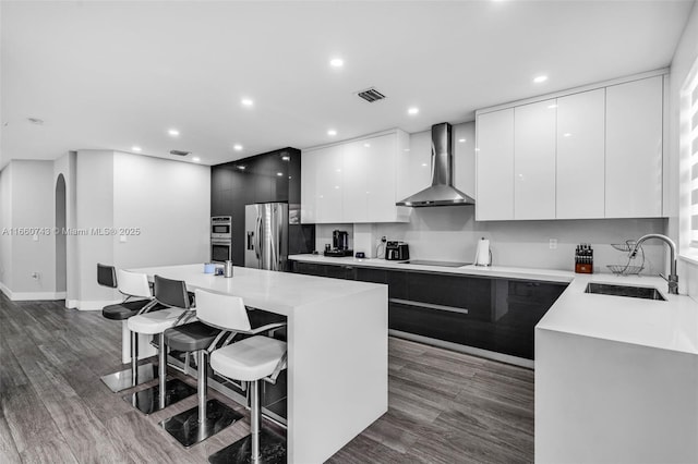 kitchen with stainless steel fridge, a kitchen breakfast bar, sink, wall chimney range hood, and a center island