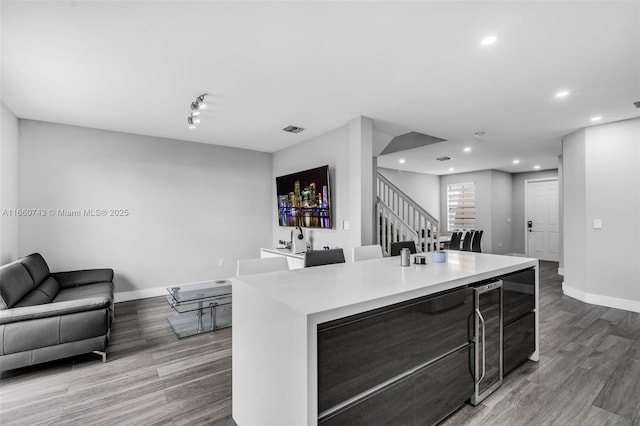 kitchen with wine cooler, a kitchen island with sink, and light wood-type flooring