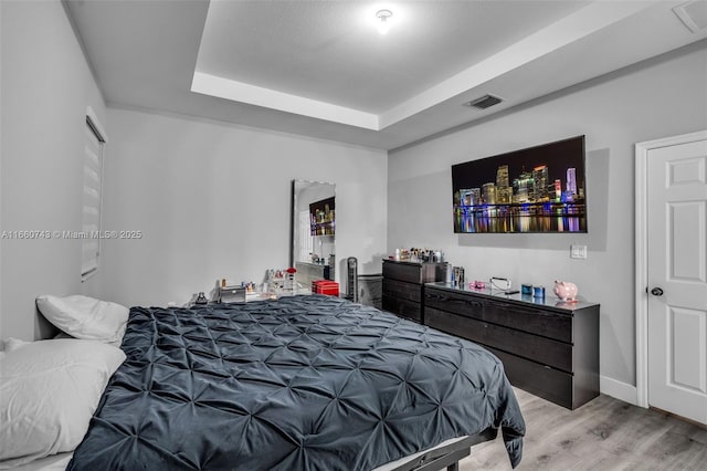 bedroom with light wood-type flooring and a raised ceiling