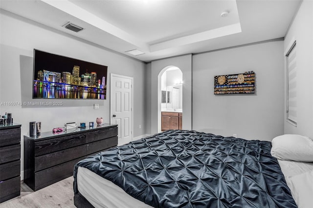 bedroom featuring connected bathroom, a tray ceiling, and hardwood / wood-style flooring