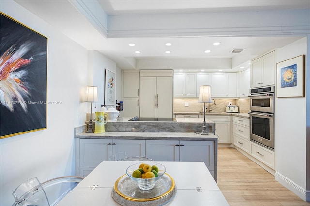 kitchen with white cabinets, double oven, light wood-type flooring, and decorative backsplash