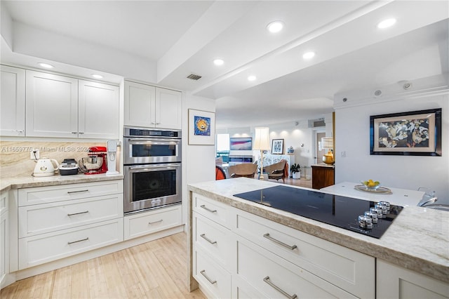 kitchen featuring white cabinets, tasteful backsplash, black electric cooktop, stainless steel double oven, and light wood-type flooring