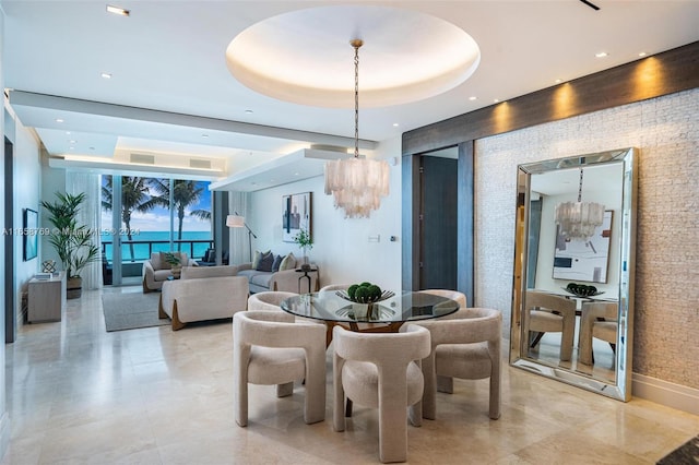 dining room with a water view, an inviting chandelier, and a raised ceiling