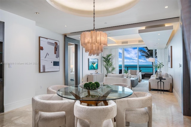 dining room featuring a notable chandelier, a water view, and a raised ceiling