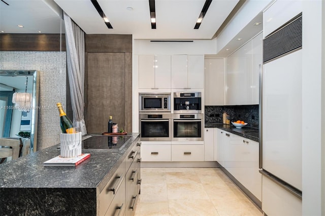 kitchen featuring white cabinets, dark stone countertops, built in appliances, and backsplash