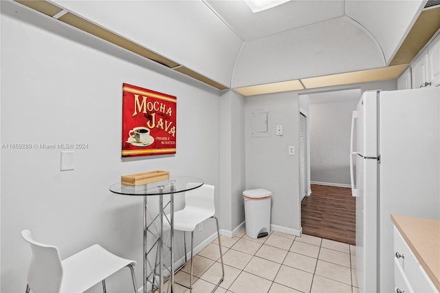 kitchen featuring light tile patterned floors, white refrigerator, vaulted ceiling, and white cabinetry