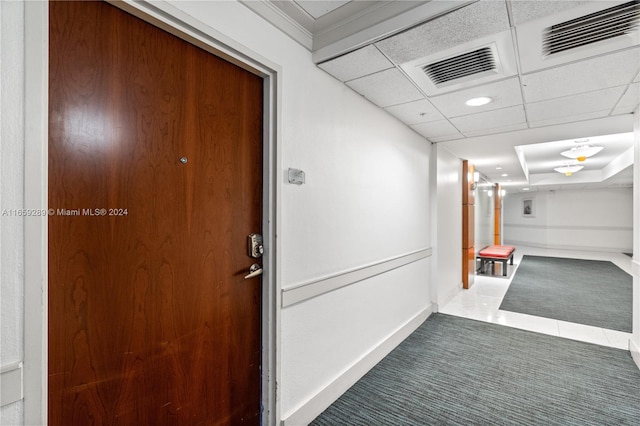 hall with tile patterned flooring, crown molding, and a paneled ceiling