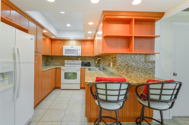 kitchen featuring decorative backsplash, white appliances, kitchen peninsula, a breakfast bar area, and sink