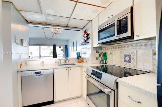 kitchen featuring a chandelier, sink, white cabinets, backsplash, and appliances with stainless steel finishes