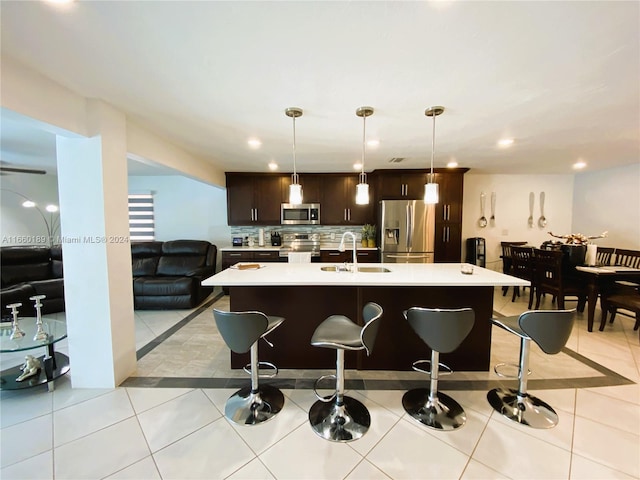 kitchen with pendant lighting, sink, dark brown cabinets, a kitchen island with sink, and stainless steel appliances