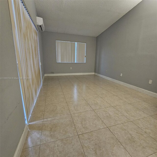 spare room featuring a wall mounted AC, a textured ceiling, and light tile patterned floors