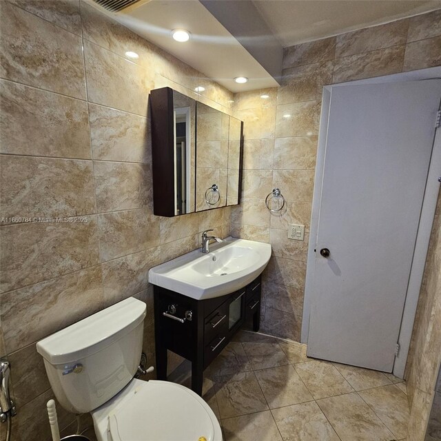 bathroom featuring vanity, toilet, and tile walls