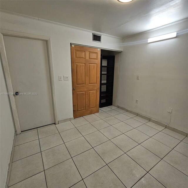 unfurnished bedroom with light tile patterned floors, ornamental molding, and a closet