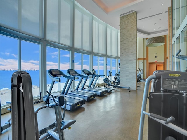 workout area featuring a towering ceiling, a water view, and a healthy amount of sunlight