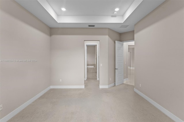 unfurnished bedroom featuring connected bathroom, a tray ceiling, and light colored carpet