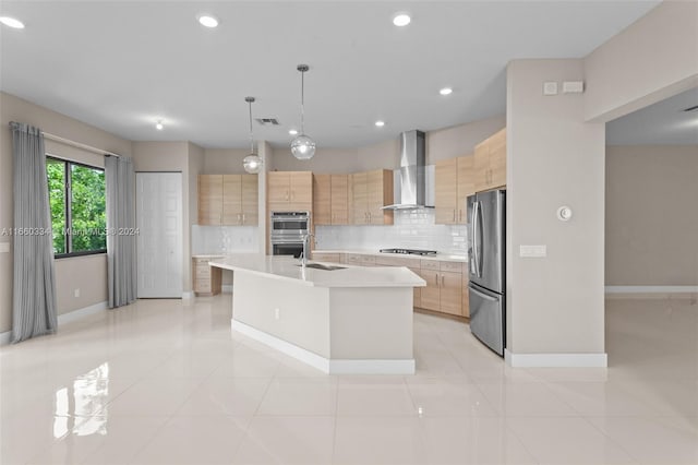 kitchen featuring appliances with stainless steel finishes, hanging light fixtures, an island with sink, light brown cabinets, and wall chimney range hood