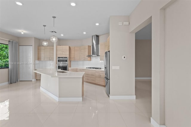 kitchen with light brown cabinets, hanging light fixtures, a kitchen island with sink, wall chimney range hood, and stainless steel appliances