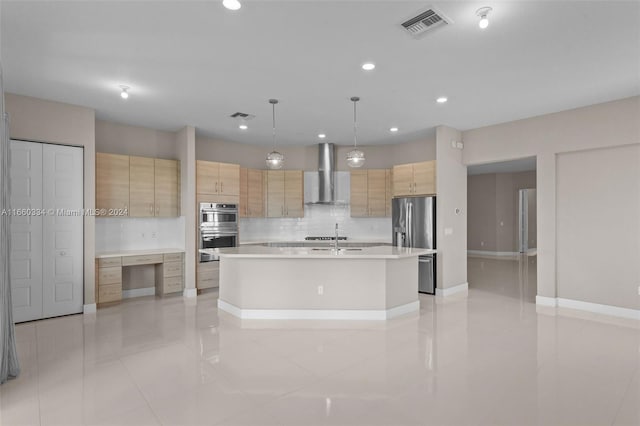 kitchen featuring light brown cabinets, an island with sink, hanging light fixtures, wall chimney exhaust hood, and backsplash