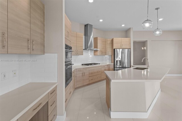 kitchen with light tile patterned flooring, an island with sink, wall chimney range hood, appliances with stainless steel finishes, and light brown cabinetry