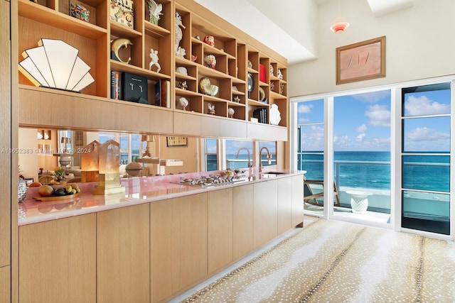 bar featuring a water view, stainless steel gas cooktop, light brown cabinets, and sink