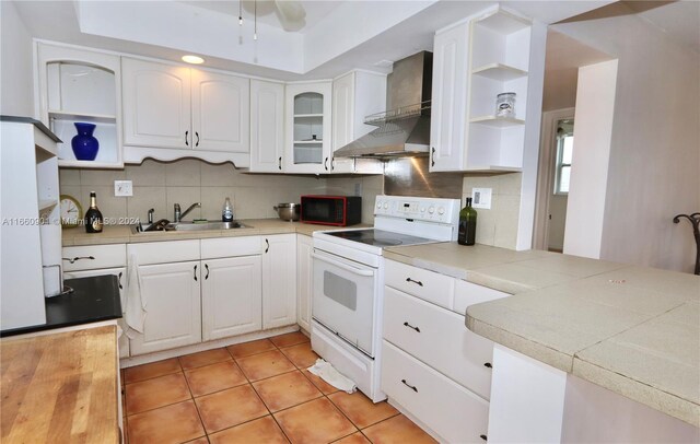 kitchen featuring sink, white cabinets, wall chimney exhaust hood, light tile patterned floors, and white range with electric cooktop