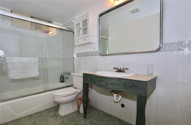 full bathroom featuring tile walls, sink, tile patterned floors, bath / shower combo with glass door, and toilet