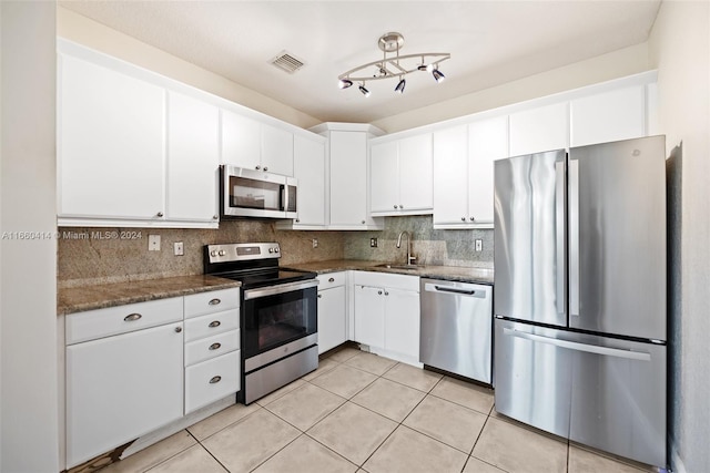 kitchen with stainless steel appliances, white cabinets, dark stone countertops, and sink