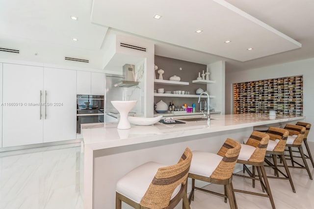 kitchen with white cabinets, sink, wall chimney range hood, and a breakfast bar