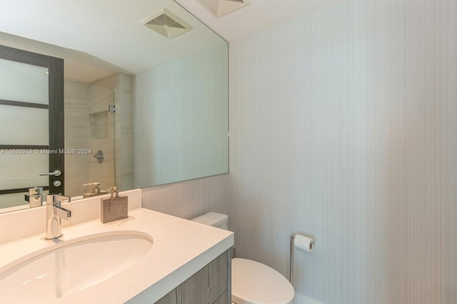 bathroom with a tile shower, vanity, and toilet