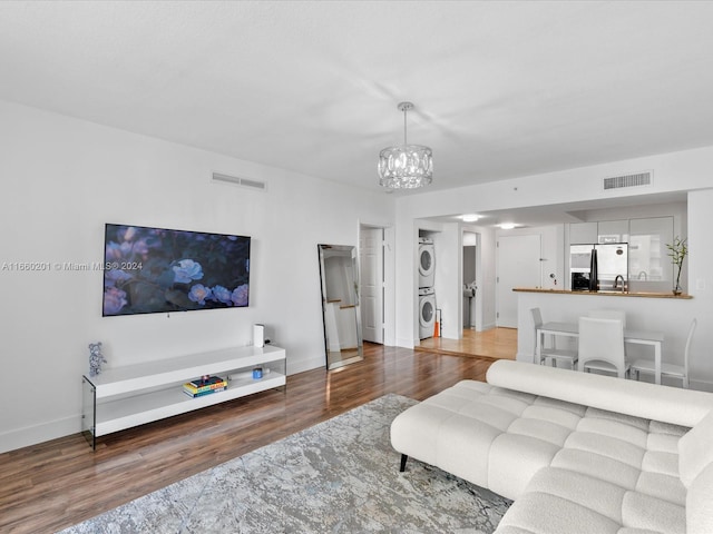 living room featuring hardwood / wood-style floors, stacked washer / dryer, and an inviting chandelier