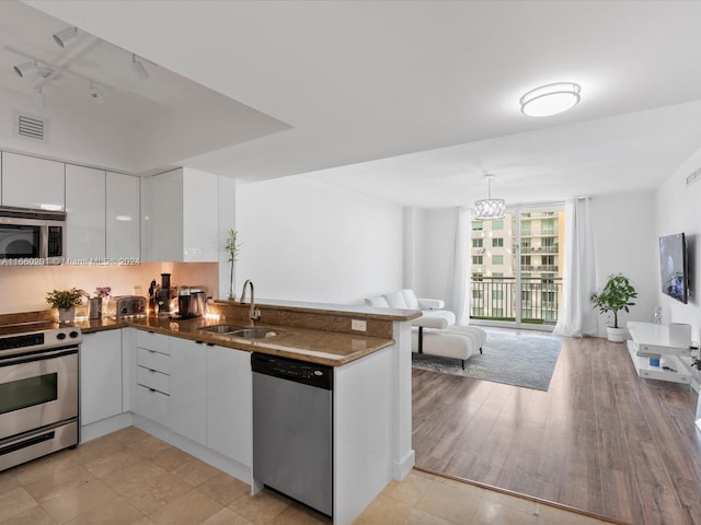 kitchen with pendant lighting, white cabinets, sink, light wood-type flooring, and stainless steel appliances