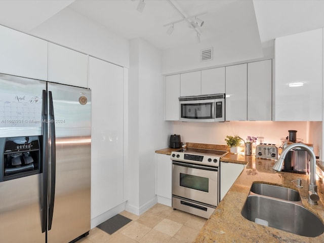 kitchen featuring track lighting, light stone counters, stainless steel appliances, sink, and white cabinetry